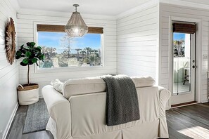 A room with a white sofa, a hanging light fixture, a large window, and a door. - Front and Sea (Port St. Joe)
