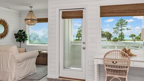 A room with a white door, a wicker chair, a white sofa, a hanging light fixture, and a view of the outdoors. - Arlanymor (Port St. Joe)