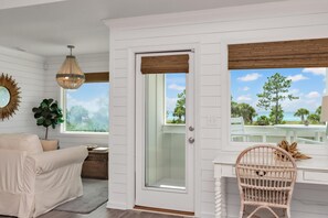 A room with a white door, a wicker chair, a white sofa, a hanging light fixture, and a view of the outdoors. - Arlanymor (Port St. Joe)