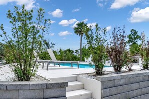 A pool area with steps leading down to the water, surrounded by various plants and white lounge chairs. - Front and Sea (Port St. Joe)