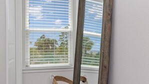 A window with white blinds, a wooden mirror leaning against the wall, and a woven basket hanging on the window. - Arlanymor (Port St. Joe)