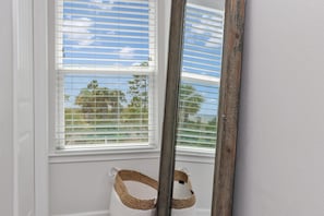 A window with white blinds, a wooden mirror leaning against the wall, and a woven basket hanging on the window. - Arlanymor (Port St. Joe)