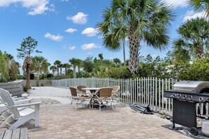 An outdoor patio with a grill, seating, and palm trees. - Front and Sea (Port St. Joe)