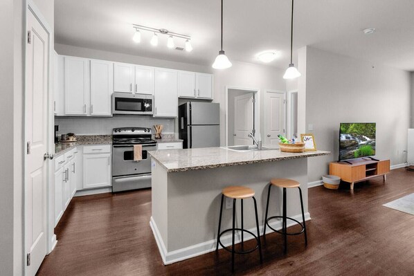 A modern kitchen with white cabinets, stainless steel appliances, and a central island with stools. - 2BR/2BA Luxury | Walkable + Parking | PET Friendly (Charlotte)