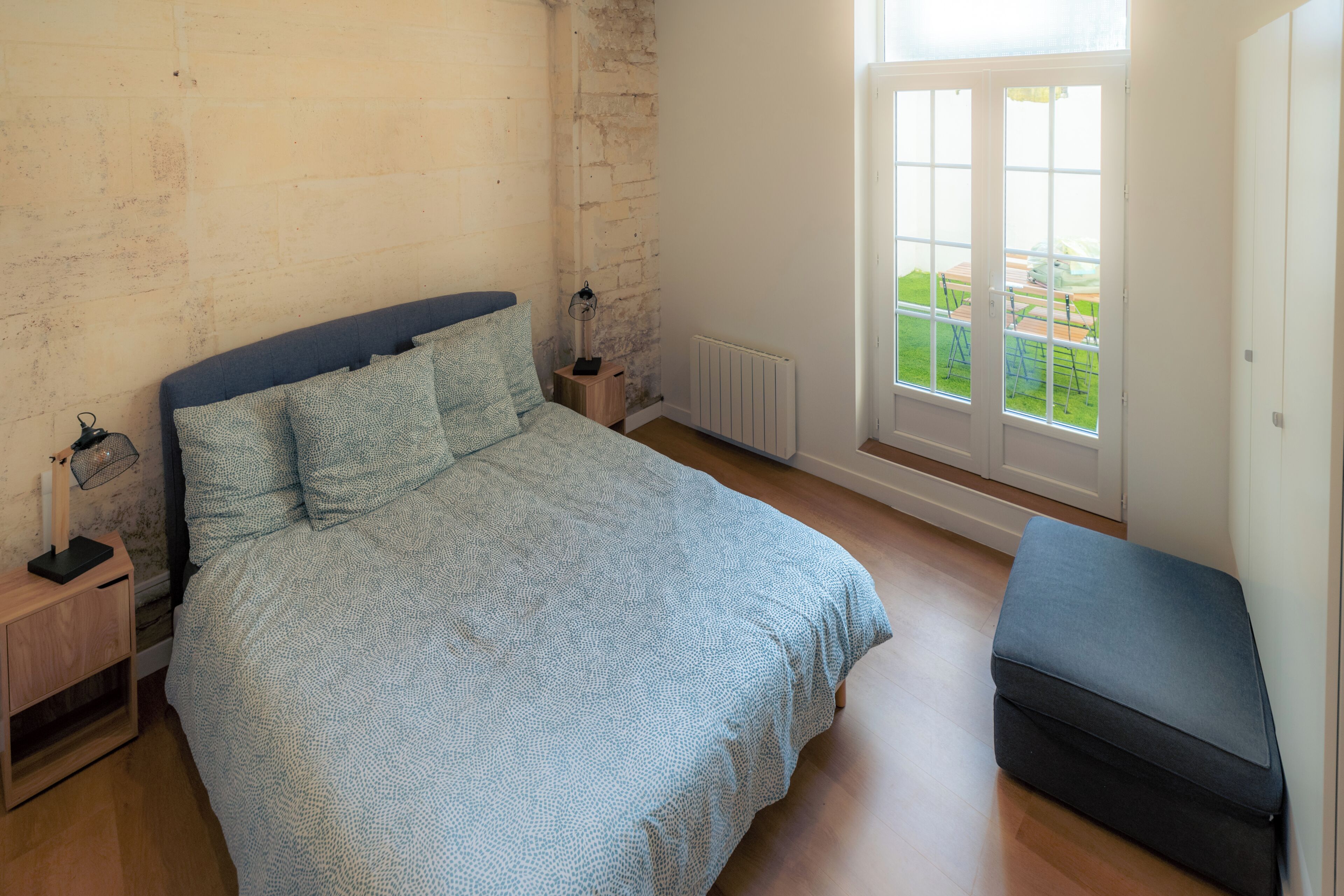 A bedroom with a bed, bedside tables, a bench, a window with a view, and a radiator.