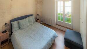 A bedroom with a bed, bedside tables, a bench, a window with a view, and a radiator. - Stunning Apartment in Old Cognac, Close to All Amenities (Cognac)