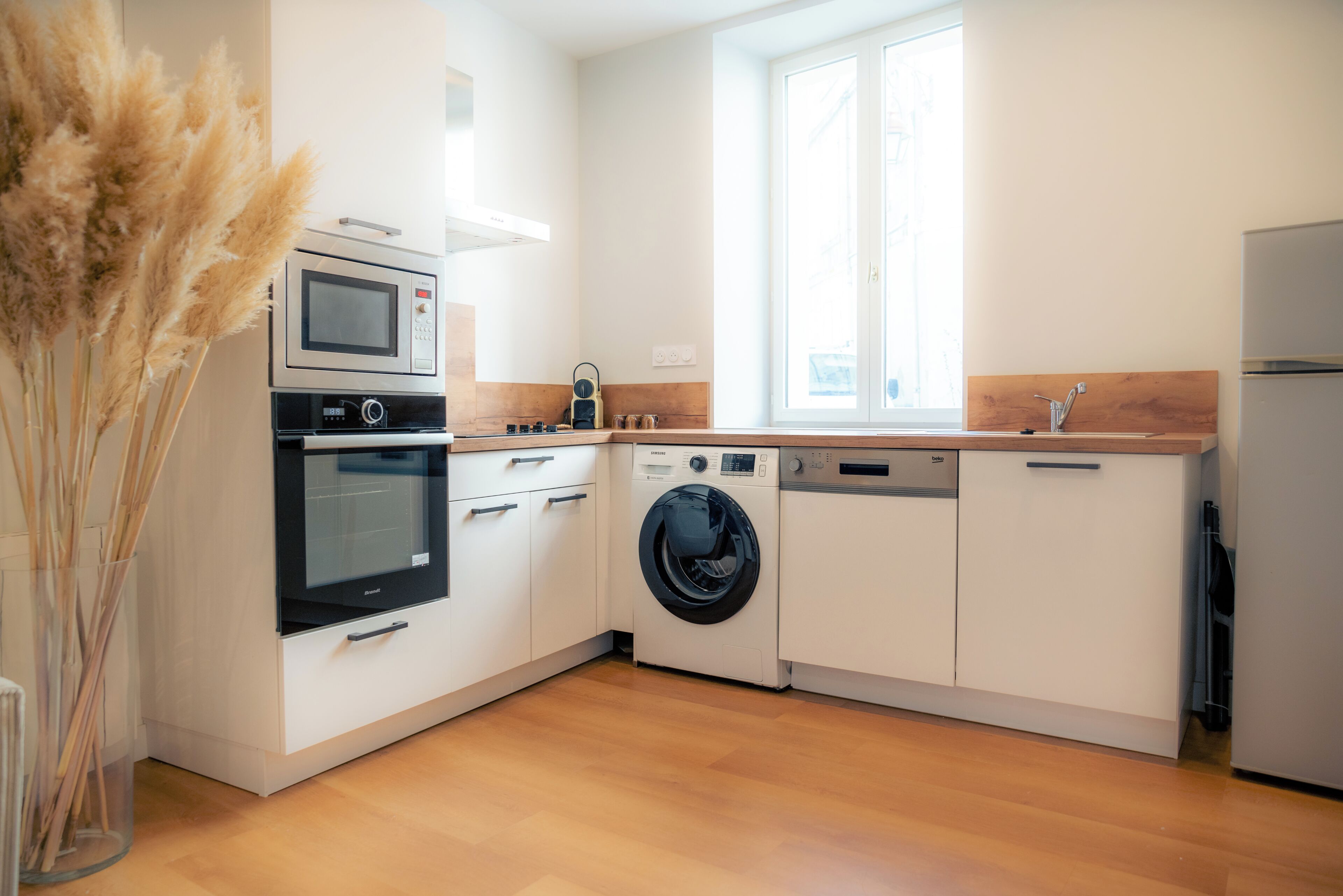 A modern kitchen with built-in appliances, a window, and a wooden countertop.