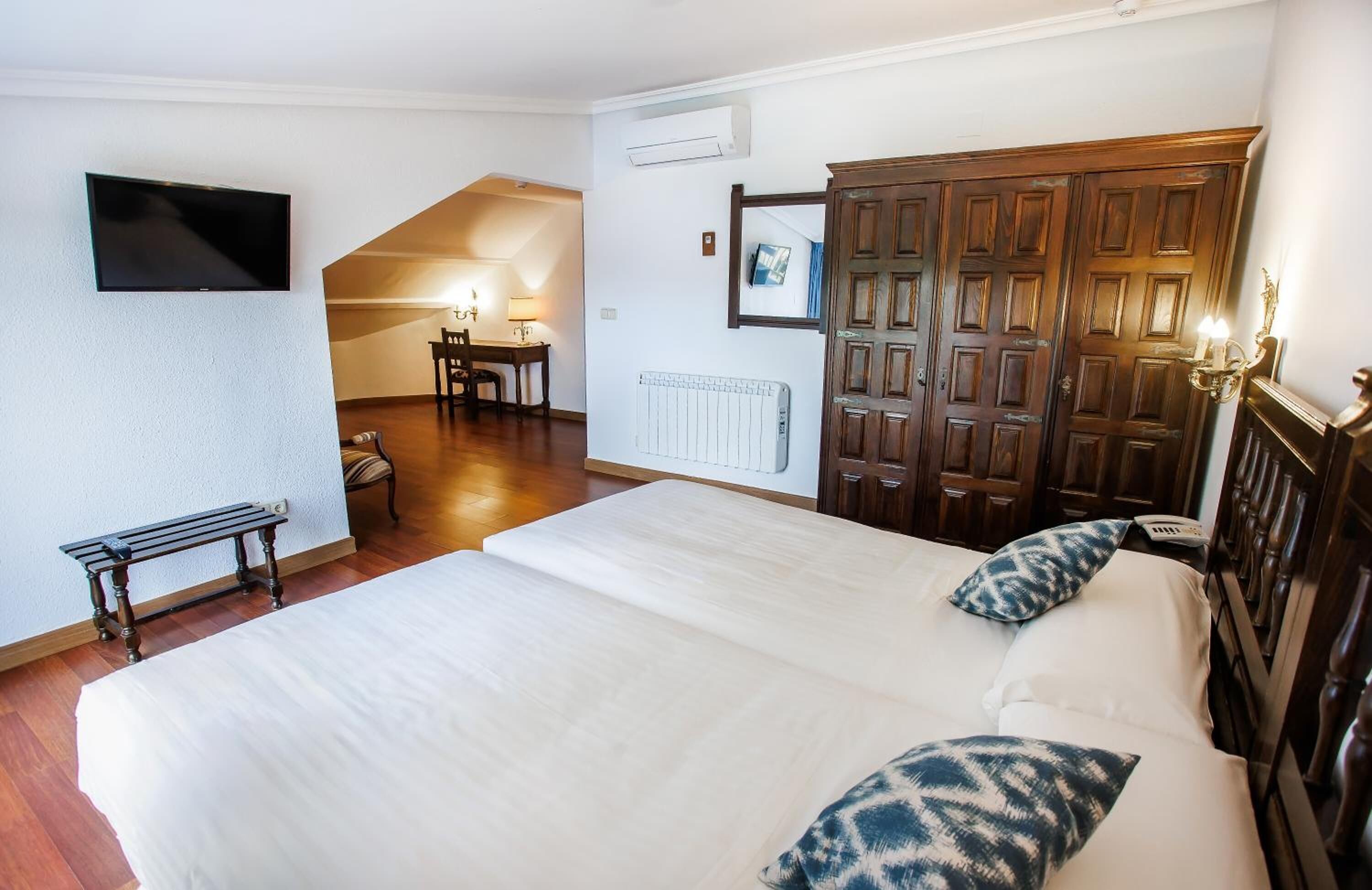 A bedroom with a large bed, a desk with a chair, a TV mounted on the wall, and a wardrobe.
