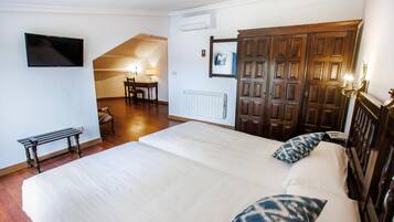 A bedroom with a large bed, a desk with a chair, a TV mounted on the wall, and a wardrobe.