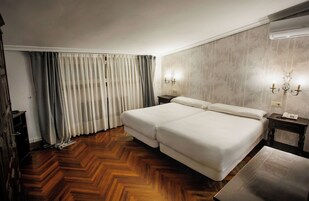 Habitación de hotel con cama doble, suelo de parqué, mesita de noche y aire acondicionado de pared.
