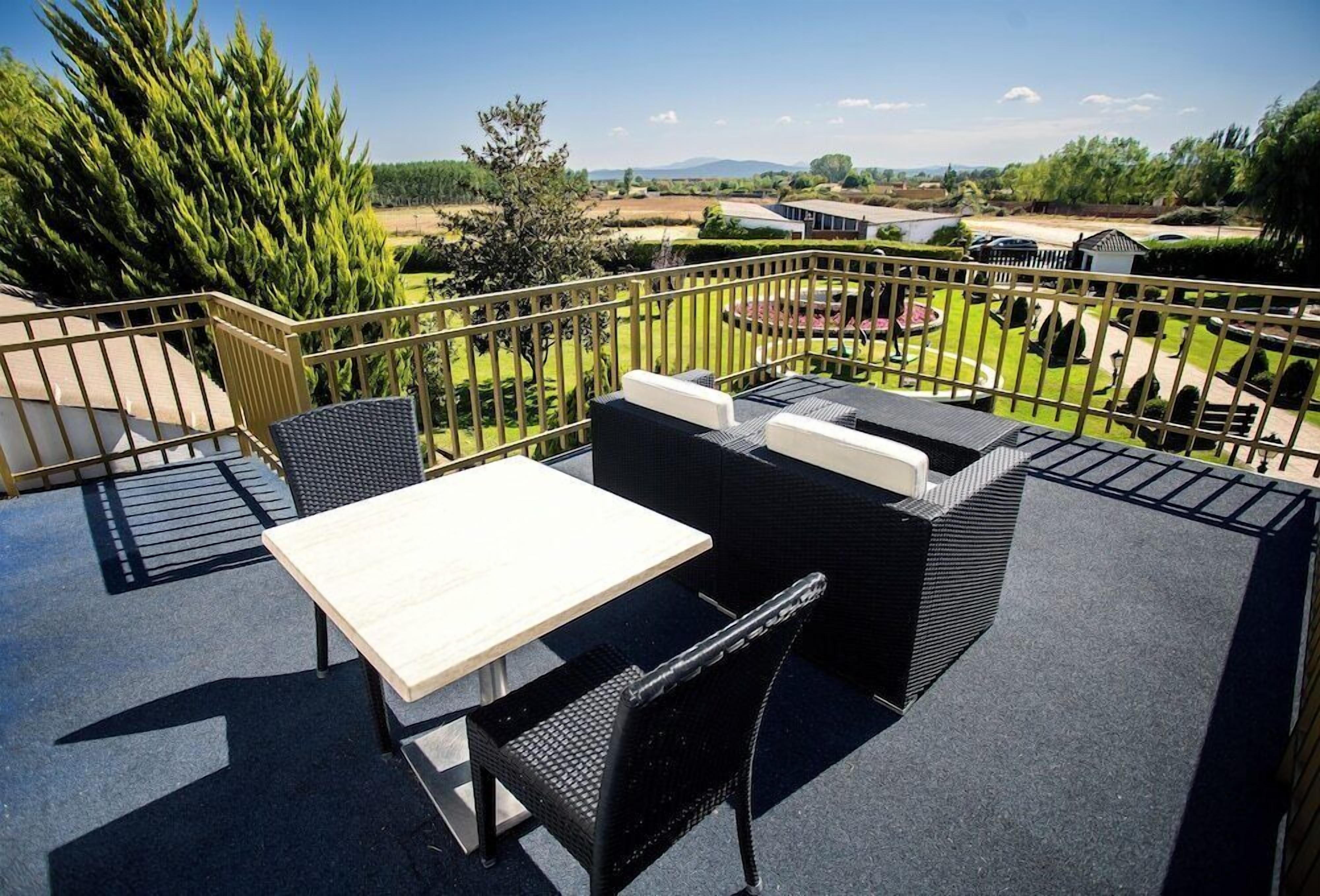 An outdoor patio with a table and chairs, a view of a landscaped garden, and a distant body of water.