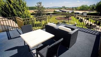 An outdoor patio with a table and chairs, a view of a landscaped garden, and a distant body of water.