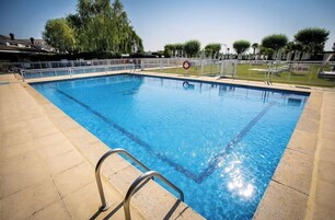Piscina rectangular con superficie de agua azul cristalina, rodeada por un deck de baldosas y una barandilla de seguridad metálica.