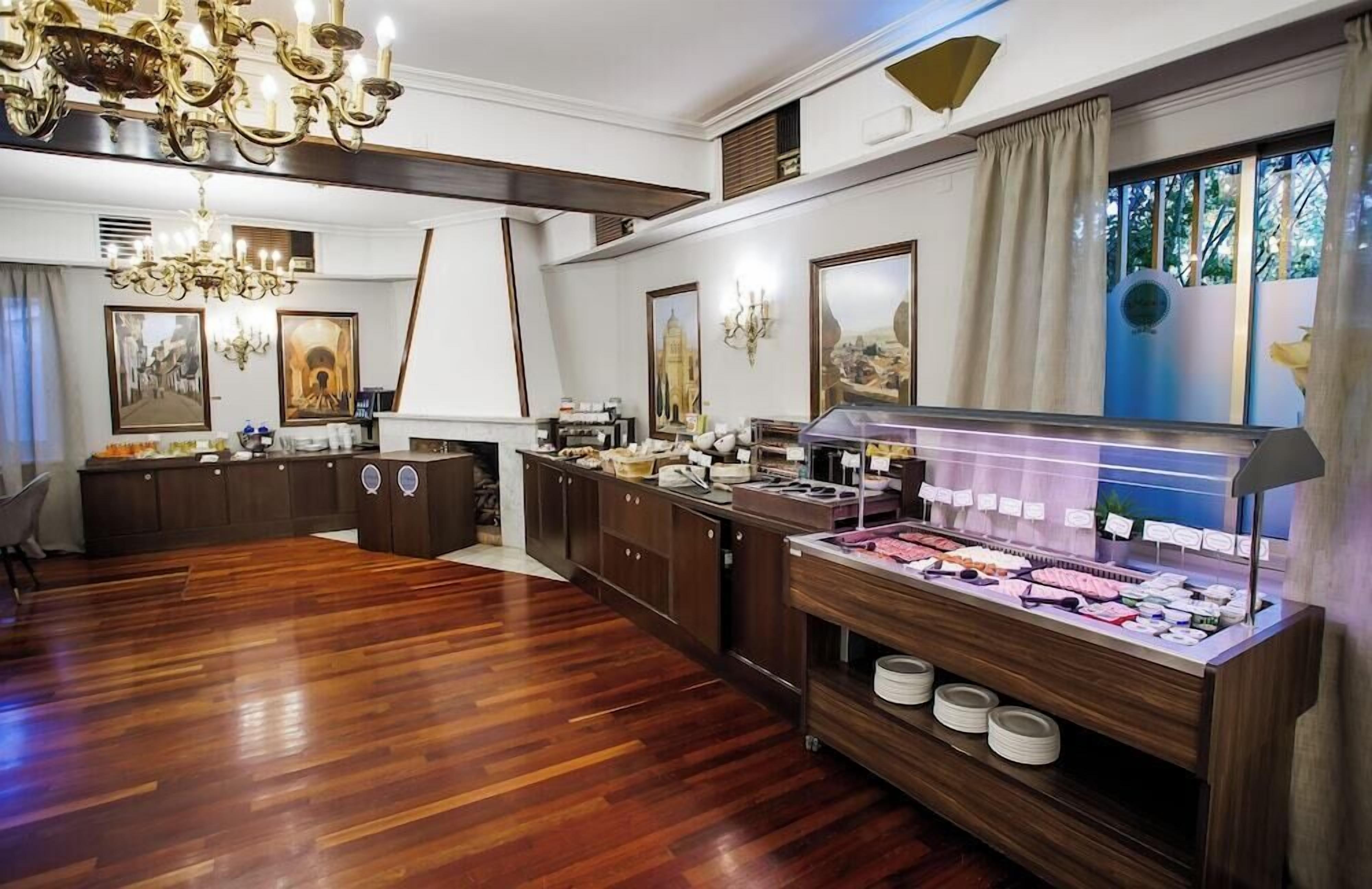 Una habitación amplia con piso de madera, un mostrador de buffet con diversas opciones de comida, un candelabro y cuadros enmarcados en las paredes.