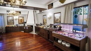 Una habitación amplia con piso de madera, un mostrador de buffet con diversas opciones de comida, un candelabro y cuadros enmarcados en las paredes.