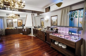 Una habitación amplia con piso de madera, un mostrador de buffet con diversas opciones de comida, un candelabro y cuadros enmarcados en las paredes.