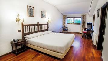 Un dormitorio con cama de madera, una mesita de noche, una silla, un escritorio con una computadora y una ventana con cortinas.
