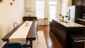 A modern kitchen with a dining area, featuring a marble countertop, stainless steel appliances, and a dining table with chairs.