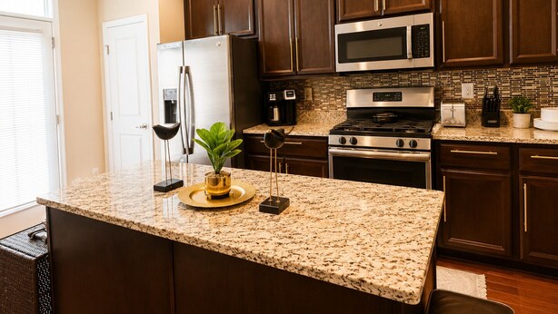 A kitchen with dark wood cabinets, stainless steel appliances, granite countertops, and a small island with a plant.