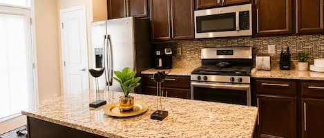 A kitchen with dark wood cabinets, stainless steel appliances, granite countertops, and a small island with a plant.