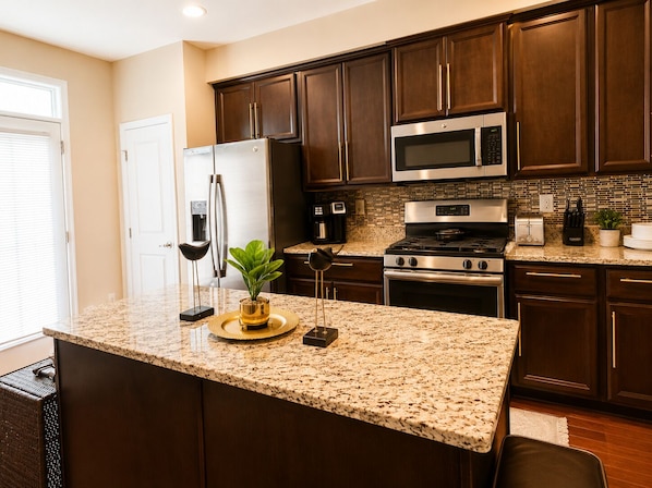 Una cocina con armarios de madera oscura, electrodomésticos de acero inoxidable, encimeras de granito y una pequeña isla con una planta.