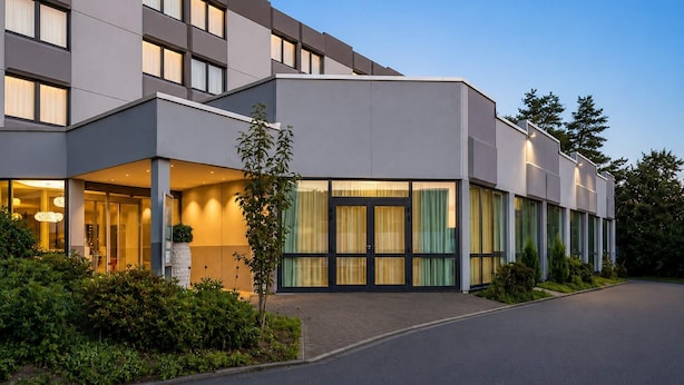 Un hotel moderno con tejado plano, amplios ventanales y un jardín cuidado.