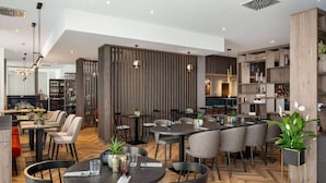 Un comedor moderno con mesas y sillas redondas, piso de madera y un panel decorativo en la pared.