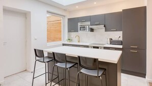 Une cuisine moderne dotée d’une verrière, de meubles de couleur sombre, d’un plan de travail blanc et de tabourets de bar.