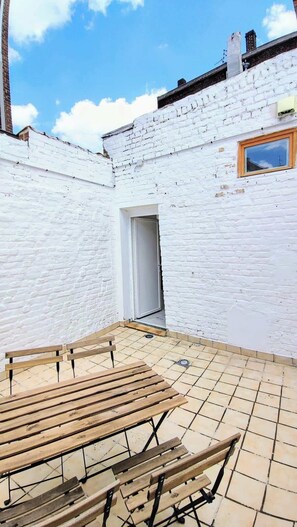 A white brick building with a tiled patio and wooden benches.
