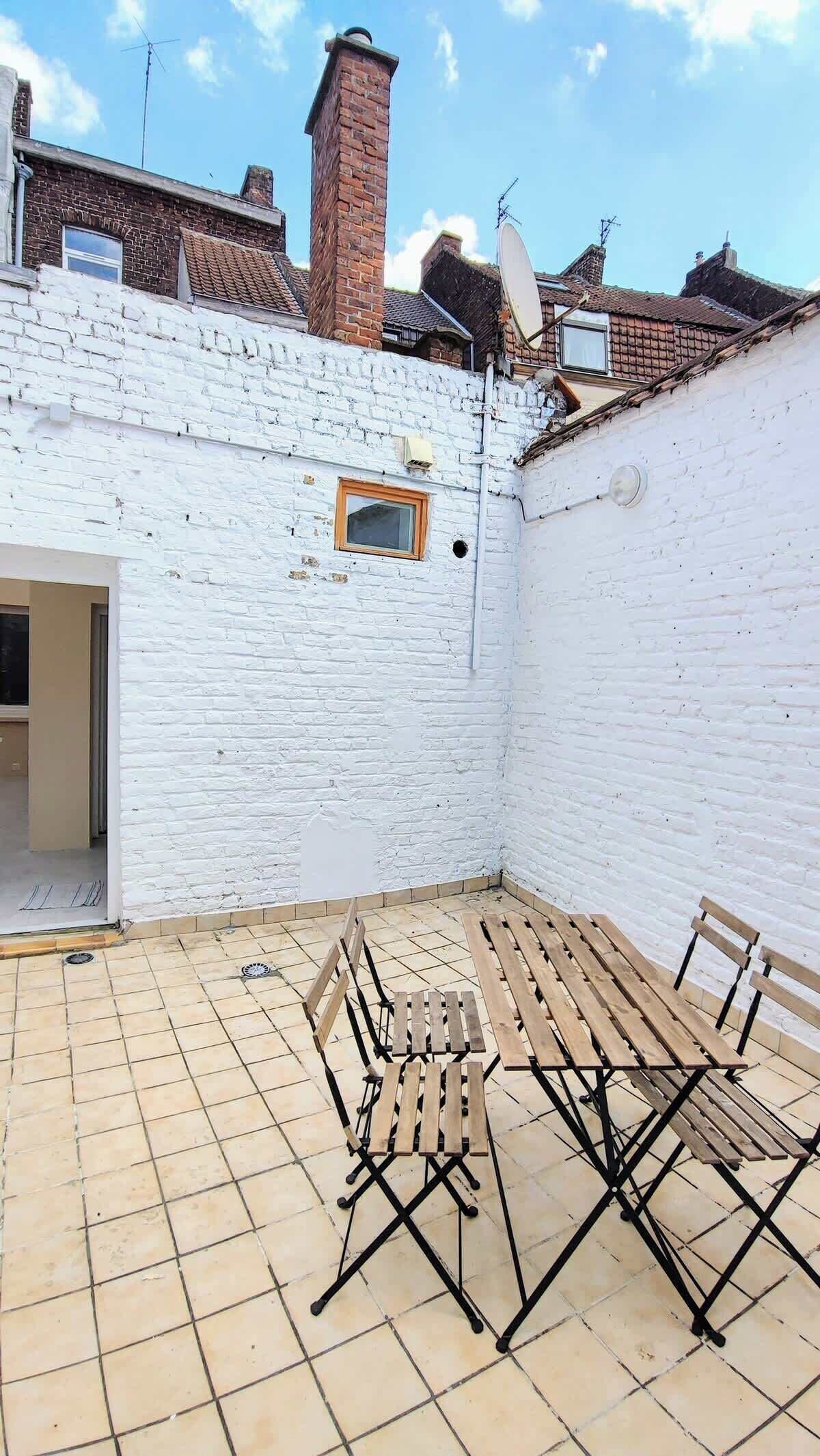 Un patio con pared de ladrillo blanco, suelo de baldosas y mobiliario de madera.