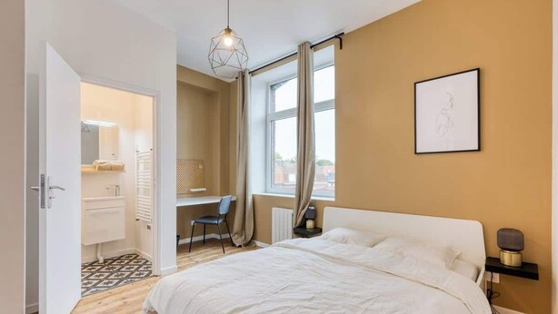 Une chambre à coucher comprenant un lit, un bureau, une chaise, une fenêtre avec des rideaux et un tableau accroché au mur.