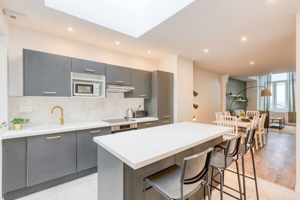 A modern kitchen with a central island, grey cabinetry, and a dining area with a table and chairs.