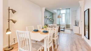 Un coin repas avec une table blanche dressée pour quatre personnes, un lampadaire et une vue sur une autre pièce avec une fenêtre.
