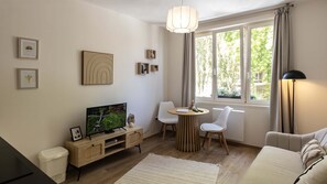 A modern living room with a TV, a dining table, chairs, a sofa, and a large window with curtains. - T2 élégant de la mairie • calme • centre (Arras)