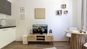 A modern living room with a flat-screen TV, a dining table, and a kitchen area with a sink and cabinets. - T2 élégant de la mairie • calme • centre (Arras)