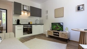Een moderne keuken met witte kastjes, een inbouwoven en een televisie op een houten standaard.