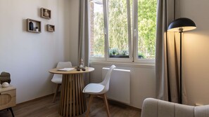 Ein Zimmer mit einem runden Holztisch, zwei weißen Stühlen, einer Stehlampe und einem Fenster mit Vorhängen.
