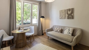 A modern living room with a sofa, two chairs, a round table, and a floor lamp. - T2 élégant de la mairie • calme • centre (Arras)