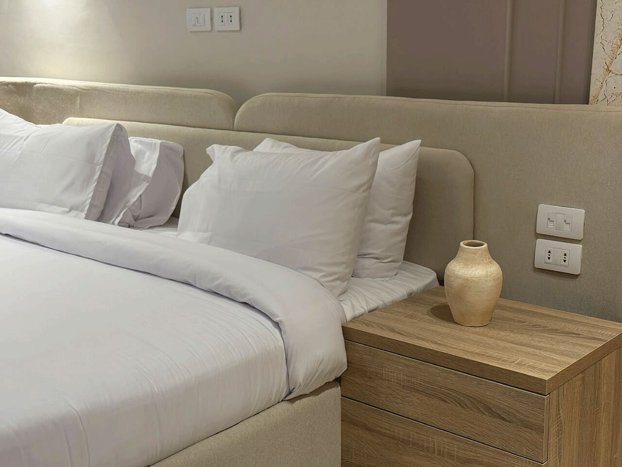 Una habitación de hotel con una cama, una mesita de noche y un jarrón.