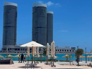 A beachfront resort with two tall buildings, outdoor seating, and umbrellas.