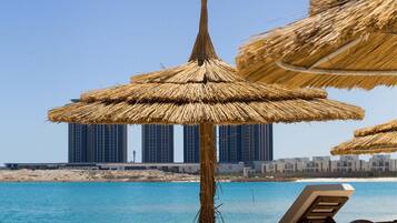A beach with thatched umbrellas, lounge chairs, and a view of high-rise buildings in the background.