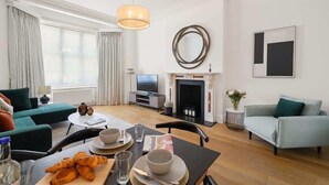 A modern living room with a sofa, a dining table with plates and glasses, a TV, and a fireplace. - HS1 - Stylish 3-Bed near Kensington High Street (Greater London)