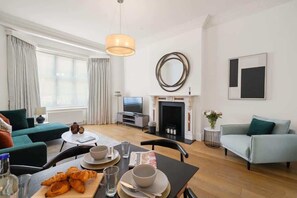 Ett modernt vardagsrum med en soffa, ett matbord med tallrikar och glas, en tv och en öppen spis.