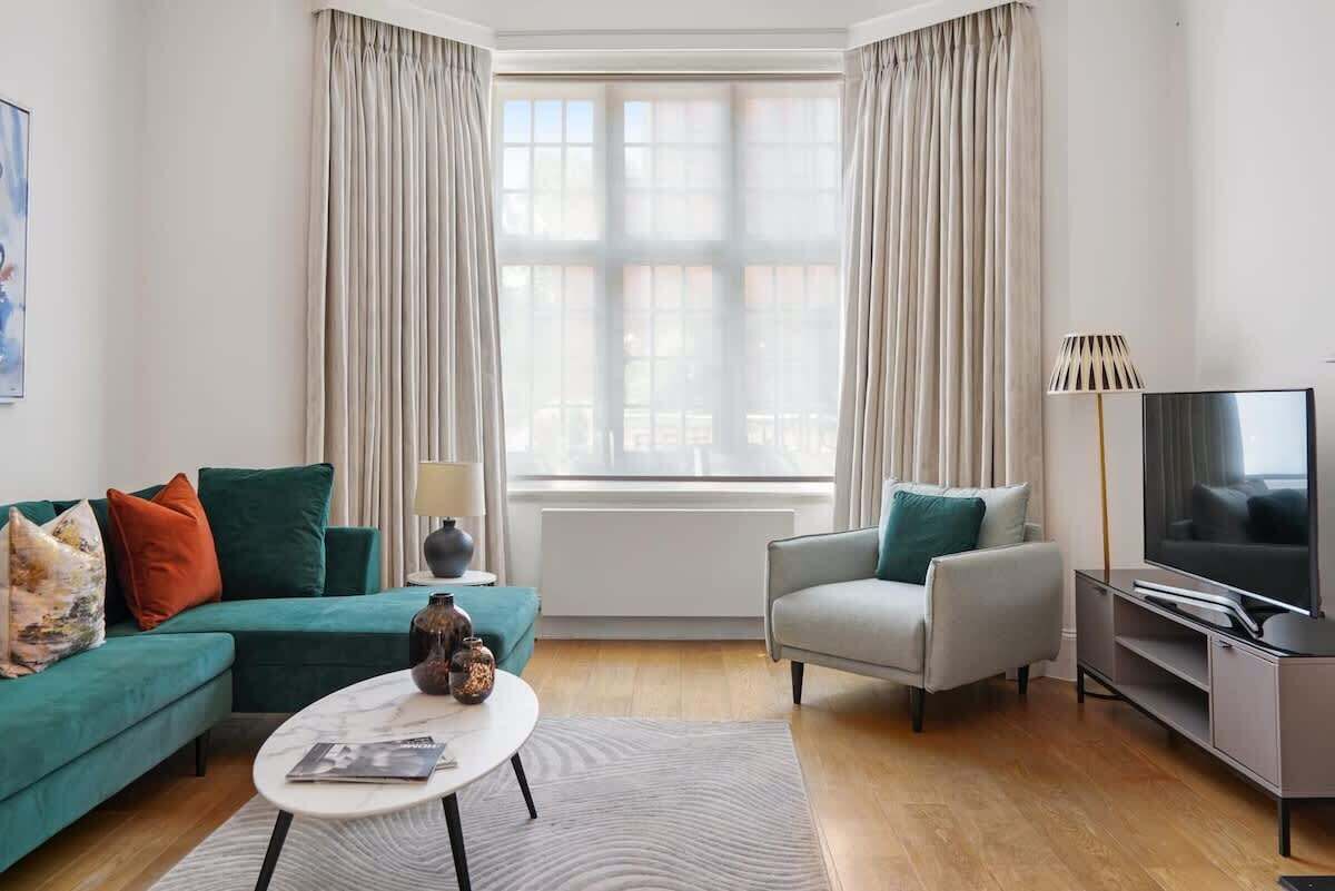 A modern living room with a sofa, armchair, coffee table, TV, and curtains.