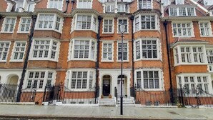 A row of red brick townhouses with bay windows, a black metal fence, and a clear sky. - HS1 - Stylish 3-Bed near Kensington High Street (Greater London)