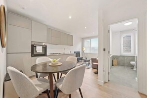 Eine moderne Küche mit Einbaugeräten, ein Essbereich mit rundem Tisch und Stühlen sowie ein Blick ins Badezimmer.