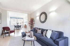 A living room with a sofa, coffee table, and a dining area in the background. - HS4 - Beautiful 2-Bed Family Apt in Kensington (Greater London)