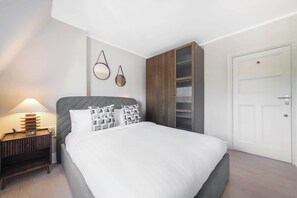A bedroom with a bed, bedside table, lamp, wardrobe, and a door. - HS4 - Beautiful 2-Bed Family Apt in Kensington (Greater London)