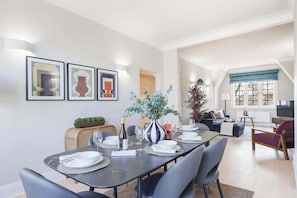 A dining area with a table set for four, a sofa, a TV, and a window with curtains. - HS4 - Beautiful 2-Bed Family Apt in Kensington (Greater London)