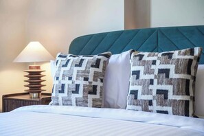 A bed with patterned pillows, a bedside lamp, and a teal headboard. - HS4 - Beautiful 2-Bed Family Apt in Kensington (Greater London)
